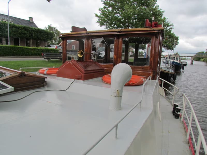 Een bovenaanzicht van het dek van een boot met een houten stuurhut, reddingsboeien en een zonnepaneel.