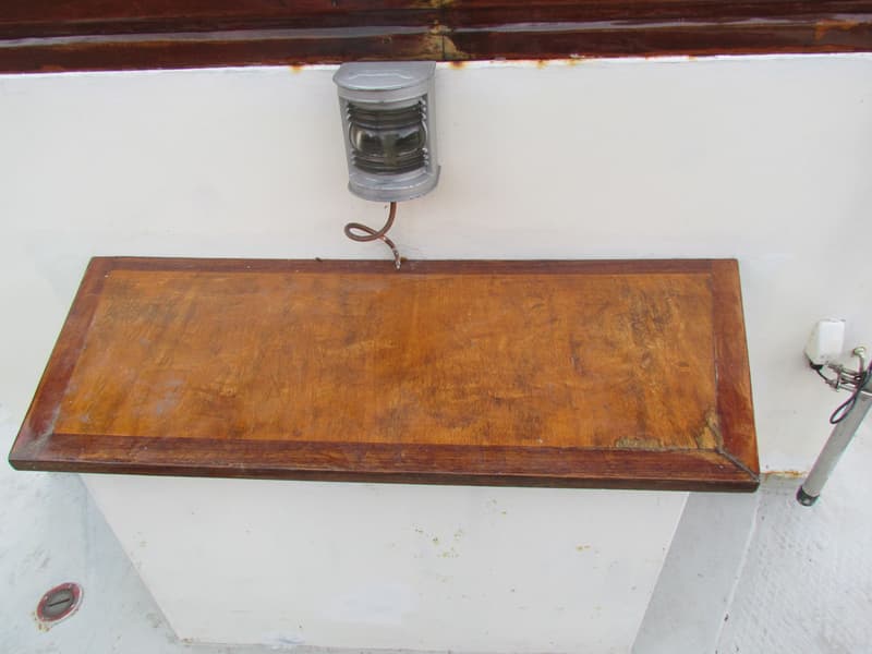 Een houten luik met een metalen lamp erboven, tegen een witte achtergrond met een bruine rand bovenaan.