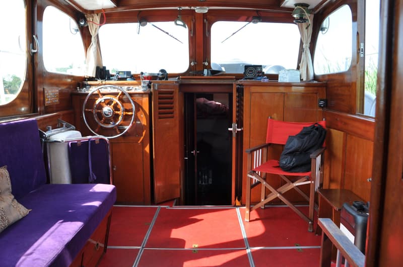 Het interieur van een boot met een houten stuurwiel, paarse bank, rode vloer en houten wanden. — Super Van Craft 1170
