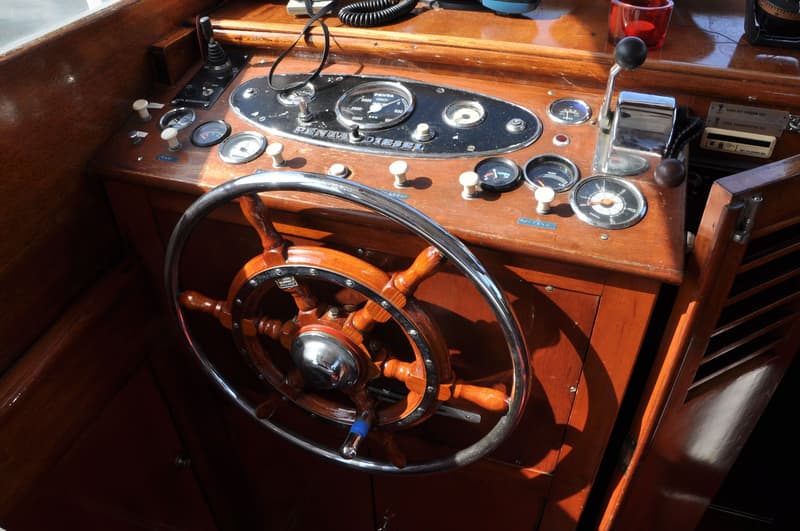 Een houten stuurwiel met een metalen rand en diverse meters en schakelaars op een houten dashboard.