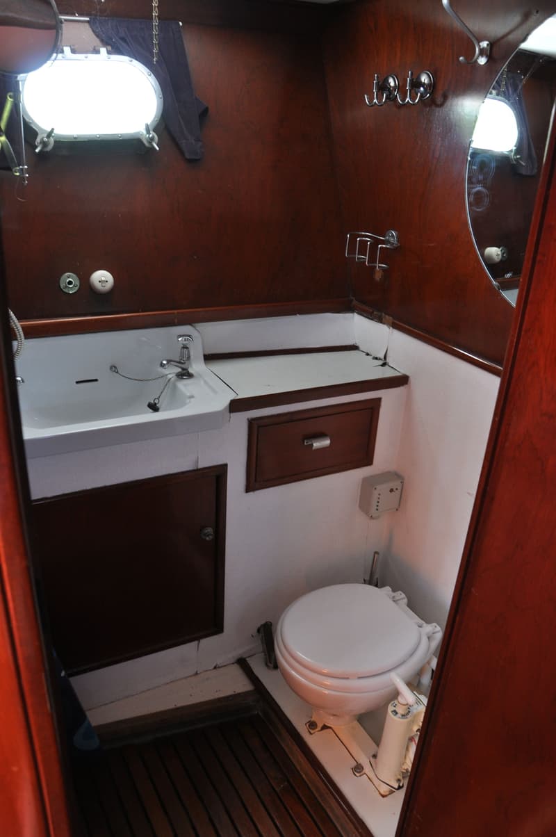 De foto toont een badkamer met een wastafel, toilet, spiegel, patrijspoort en houten lambrisering.