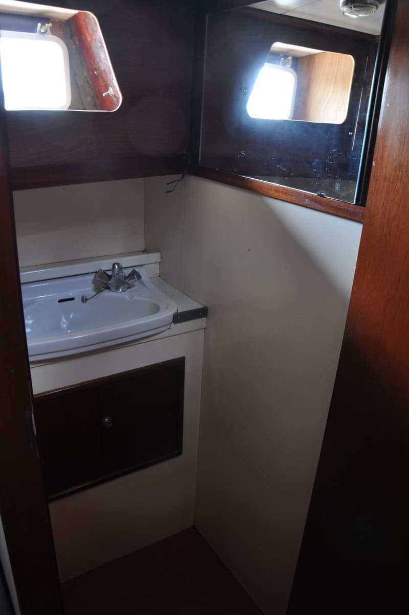 Een kleine badkamer met een witte wastafel, een kraan en een donkerbruin kastje eronder.