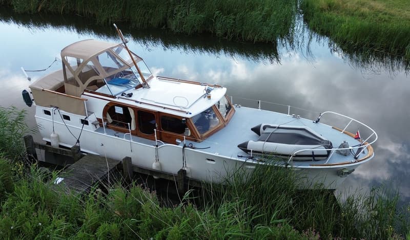 Een witte motorboot met een beige cabriokap en een rubberboot op het voordek ligt aangemeerd aan een houten steiger.