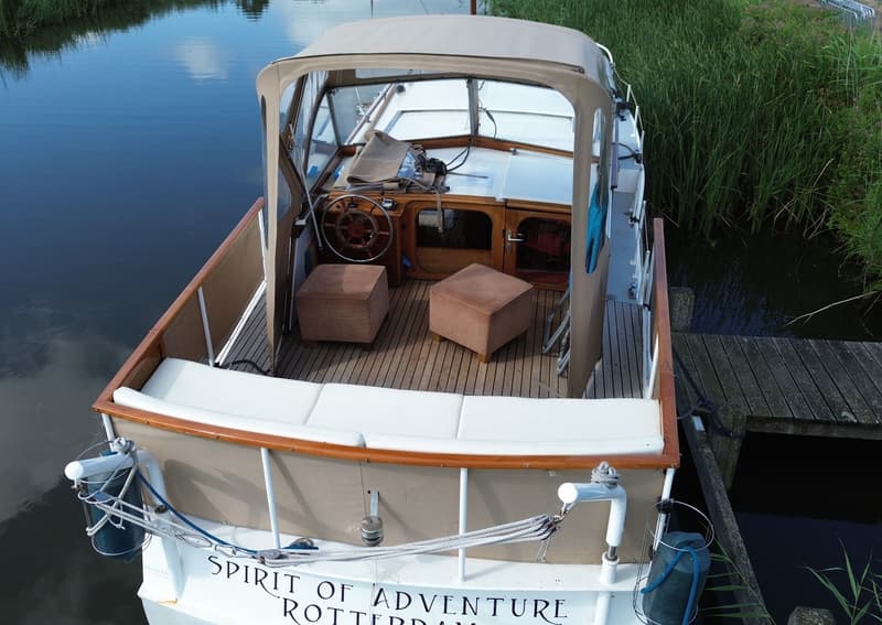 Een boot met een beige kap en houten dek ligt aangemeerd aan een houten steiger, omringd door riet. — Super Van Craft 1170