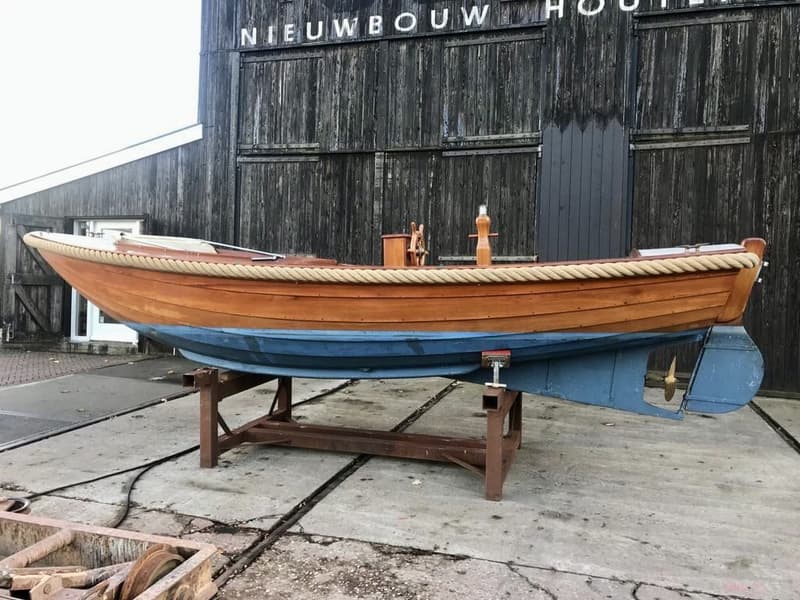 Een houten boot met een blauwe onderkant staat op een bok voor een donkerhouten gebouw met de tekst "NIEUWBOUW" erop.