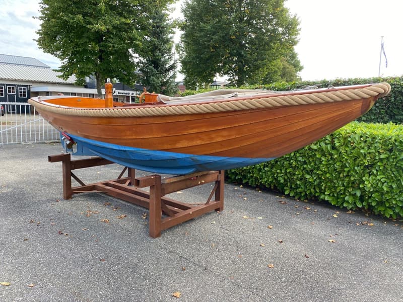 Een houten boot met een blauwe onderkant staat op een bruine bok op een geasfalteerde ondergrond. — De Jong Vlet 6.20