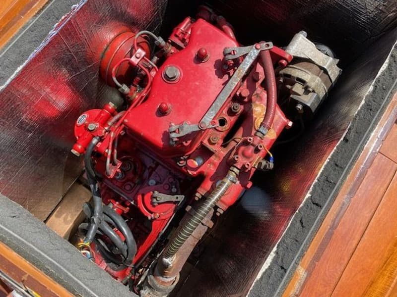 Een rode scheepsmotor is zichtbaar in een motorruimte met isolatiemateriaal en houten afwerking.
