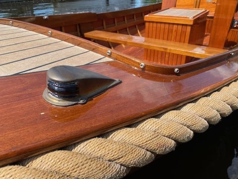 Een detailfoto van een houten boot met een navigatielicht, een touwstootrand en een teakhouten dek. — De Jongvlet 6.20