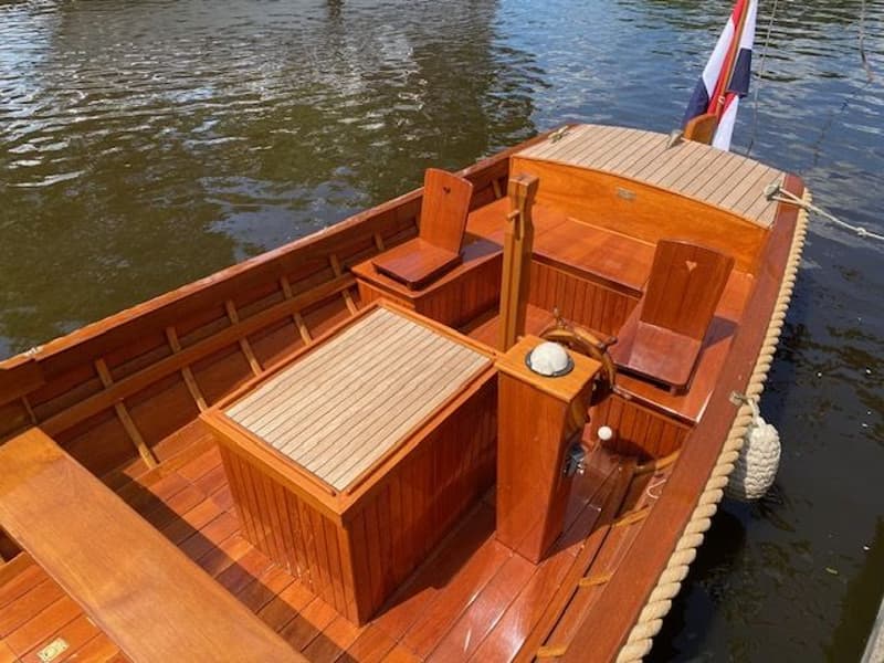 Een houten boot met een Nederlandse vlag aan de achtersteven, liggend in het water. — De Jongvlet 6.20