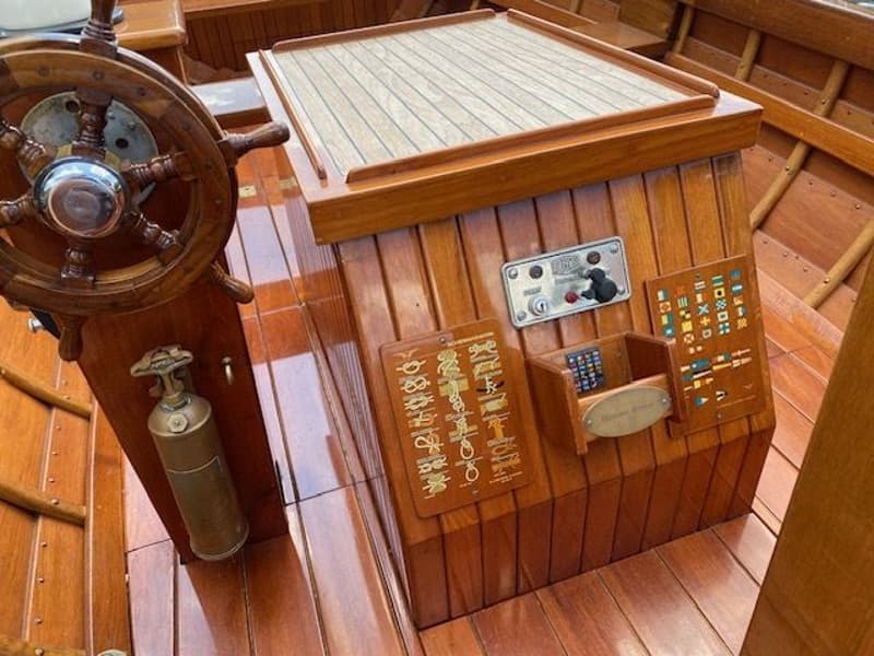 Een houten stuurwiel, een bedieningspaneel en diverse houten panelen met symbolen zijn zichtbaar in een houten boot.
