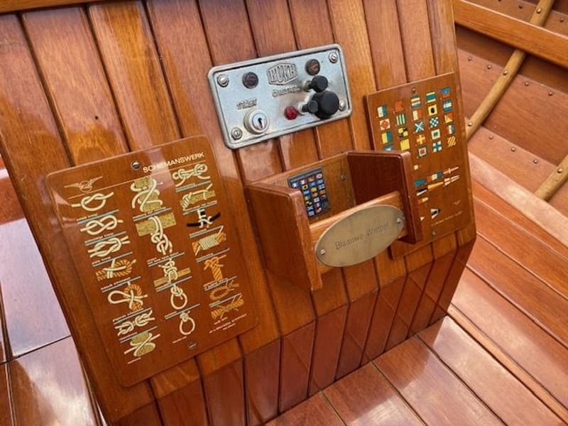 Een detailfoto van een houten bootinterieur met een bedieningspaneel, knopenkaart en vlaggenkaart.