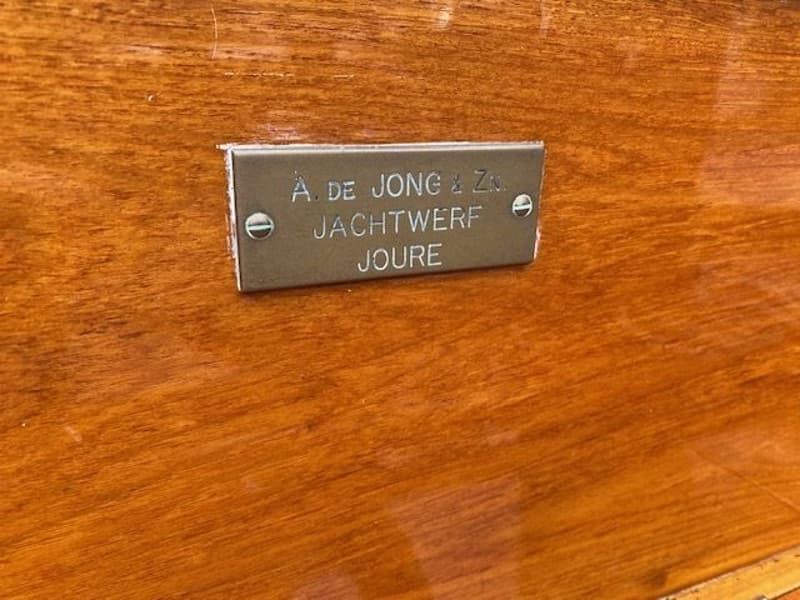 Een metalen plaatje met de tekst "A. DE JONG & Zn. JACHTWERF JOURE" is bevestigd op een houten oppervlak.