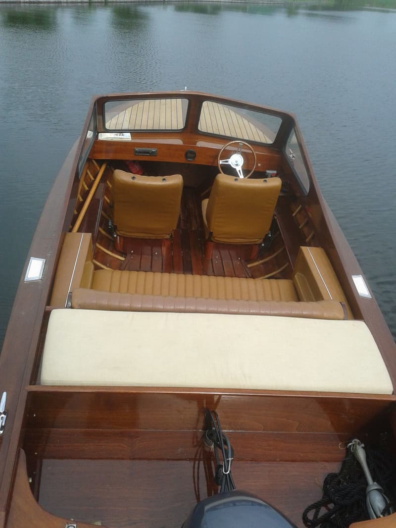 Een houten boot met bruine bekleding en een stuurwiel, liggend in het water. — Flying Finn 19.60
