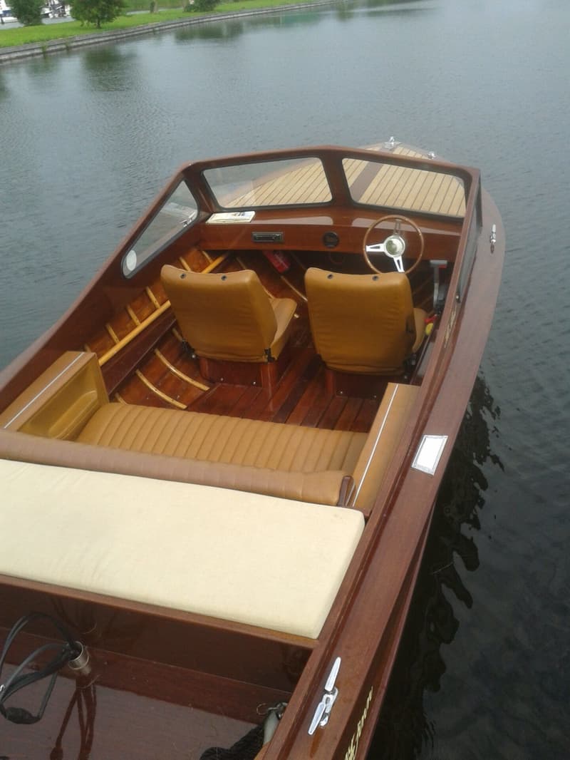 Een houten motorboot met bruine bekleding en een stuurwiel ligt in het water. — Flying Finn 19.60