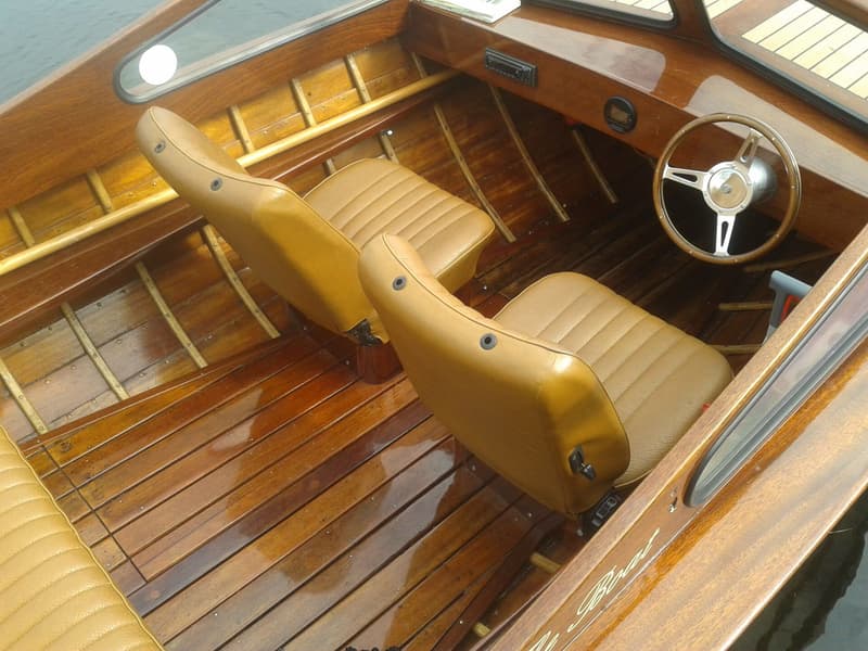 Het interieur van een houten boot met twee bruine stoelen, een stuurwiel en een dashboard. — Flying Finn 19.60