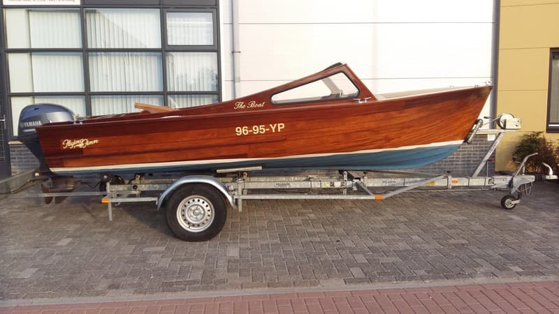 Een houten boot met de naam "The Boat" en registratienummer "96-95-YP" staat op een trailer met een Yamaha buitenboordmotor.
