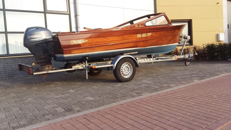 Een houten boot met een Yamaha buitenboordmotor staat op een trailer geparkeerd op een stenen oprit. — Flying Finn 19.60