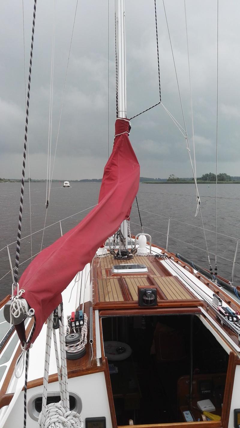 Een zeilboot met een rode zeilhoes en een kompas op het dek vaart op een meer onder een bewolkte hemel. — Waarschip 900 +