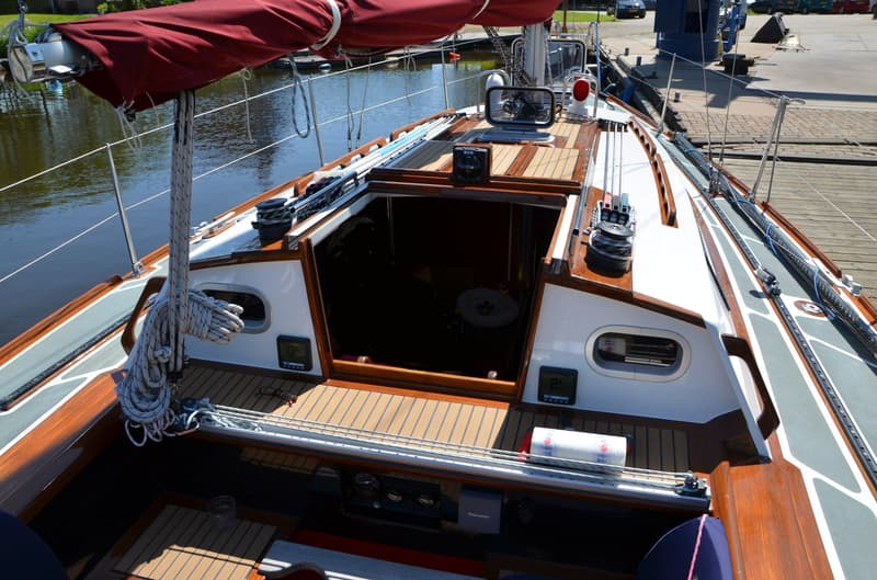 Een bovenaanzicht van een zeilboot met een open kajuitingang, een rood zeil en een houten dek. — Waarschip 900 +
