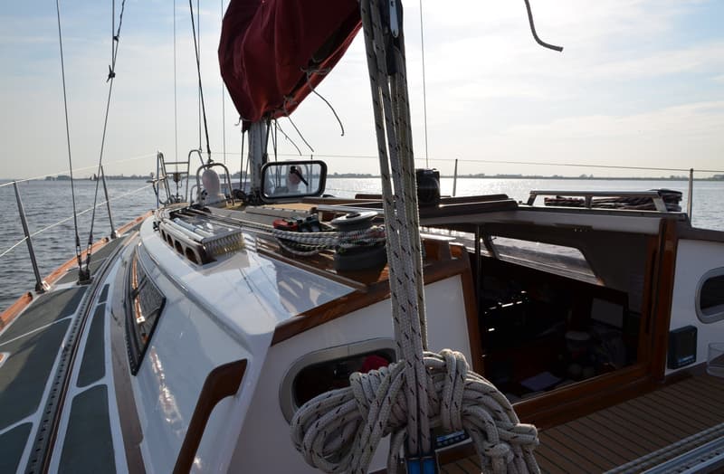 Een zeilboot met een rood zeil en een wit dek vaart op een waterlichaam onder een heldere hemel. — Waarschip 900 +