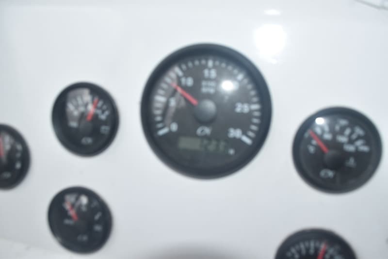 Een close-up van een wit dashboard met vijf ronde, zwarte meters, waarvan de middelste het grootst is.