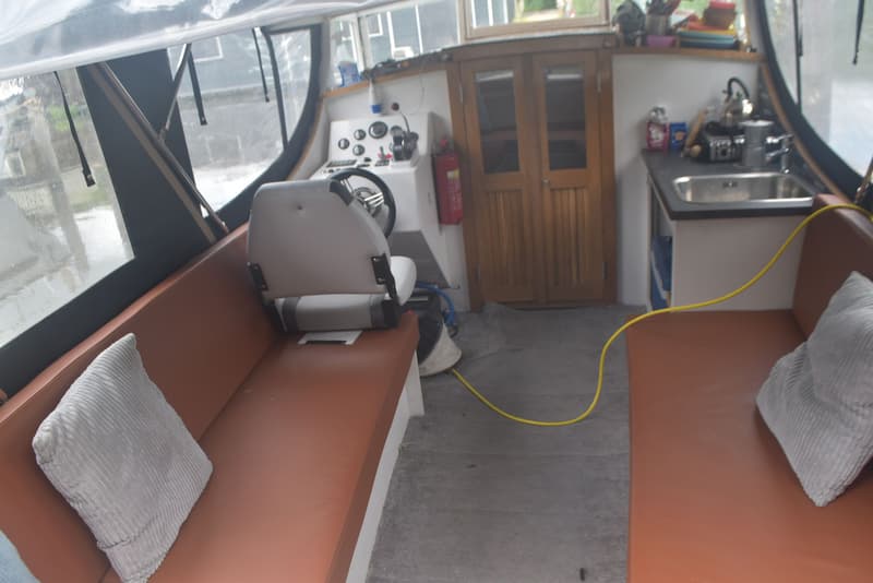 De foto toont het interieur van een boot met een stuurstand, zitbanken, een kombuis en een kajuitdeur. — 820C Steilsteven