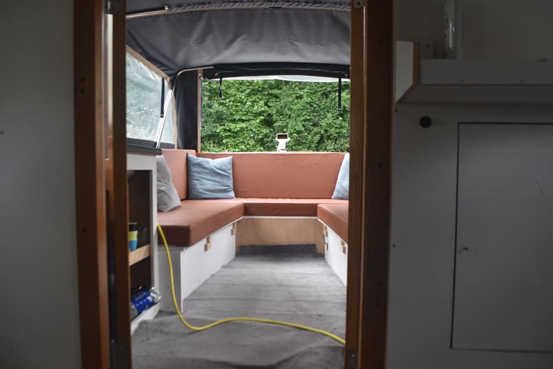 De foto toont het interieur van een boot met bruine banken, blauwe kussens en een grijs tapijt, gezien vanuit een…
