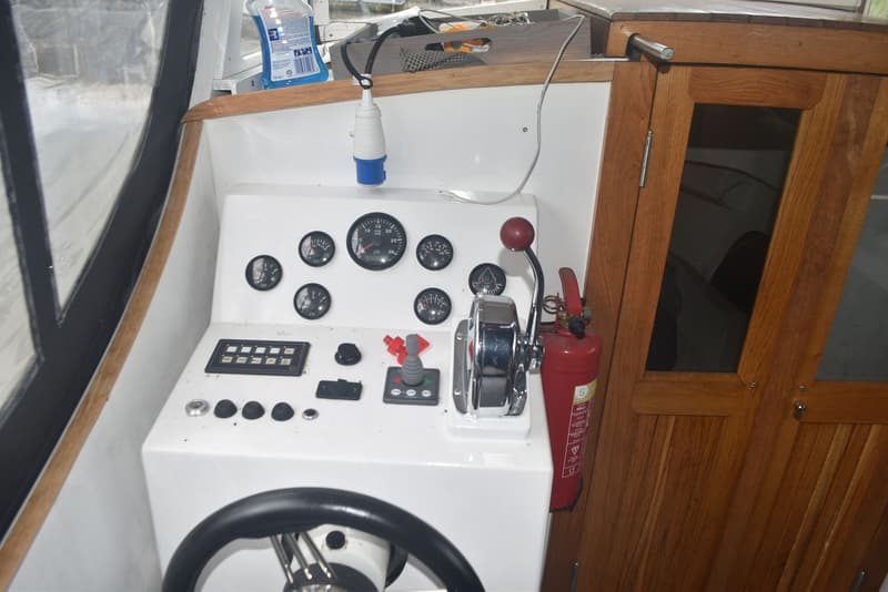 Een wit dashboard met diverse meters, schakelaars, een gashendel, een stuurwiel en een rode brandblusser.