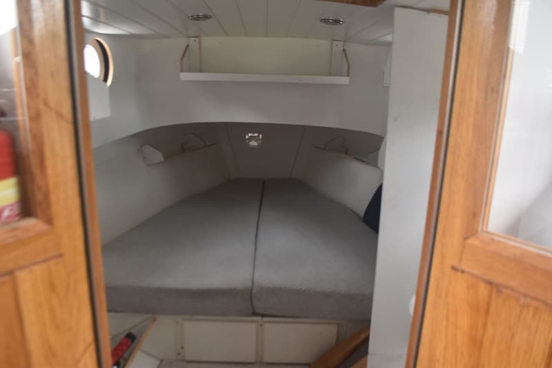 De foto toont het interieur van een kajuit met een tweepersoonsbed, een patrijspoort en houten deuren. — 820C Steilsteven