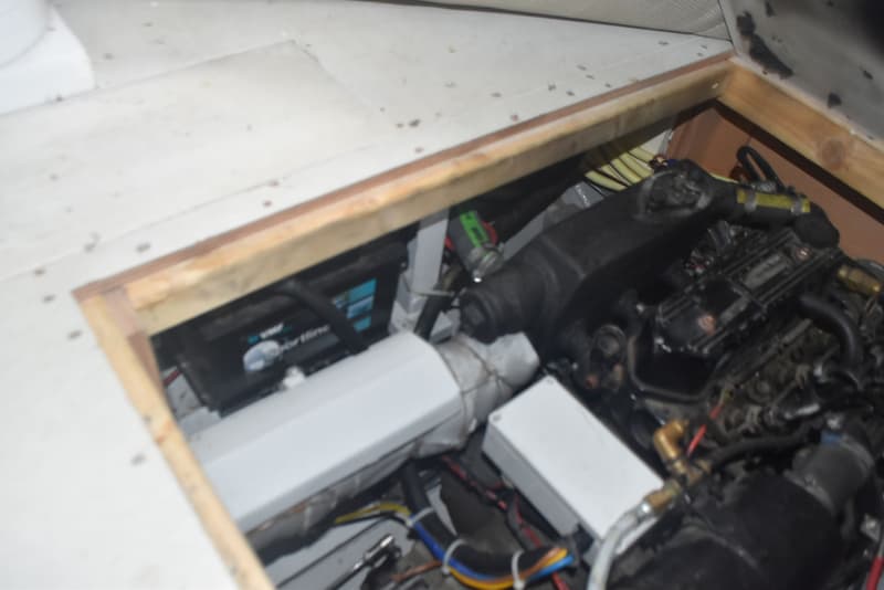 Een close-up van een motorruimte met een zwarte motor, een accu en diverse kabels en leidingen.