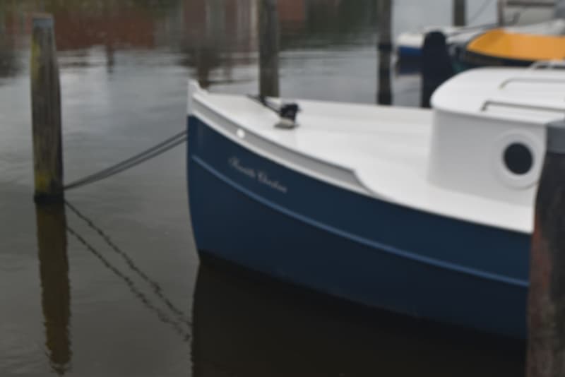 Een blauw-witte boot met de naam "Henriette Christine" ligt aangemeerd aan een houten paal. — 820C Steilsteven