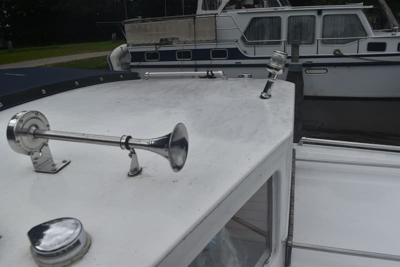 Op de foto is een deel van een wit bootdek te zien met een zilverkleurige scheepshoorn en een navigatielicht.