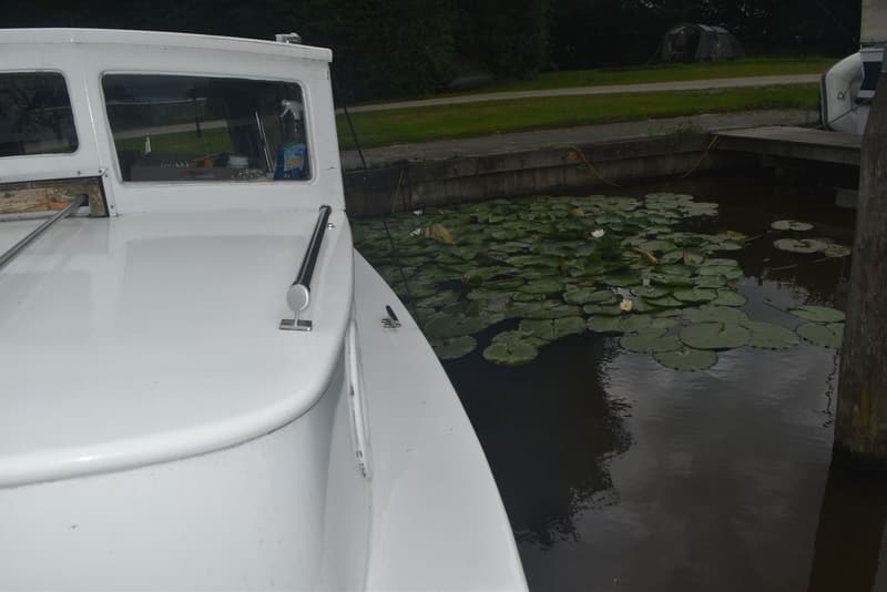 Een witte boot ligt aangemeerd naast een houten steiger, omringd door waterlelies in het water. — 820C Steilsteven