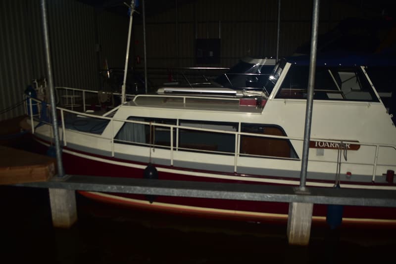 Een motorjacht met de naam "TOARKER" ligt in het water, deels zichtbaar achter een steiger.