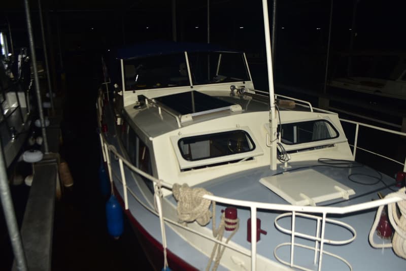 Een witte boot met een blauw dekzeil en zonnepanelen op het dak, afgemeerd in een donkere loods. — Doerak 850 AK