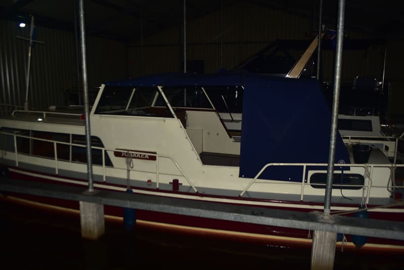 Een witte boot met een blauwe kap en rode romp ligt in het water onder een afdak. — Doerak 850 AK