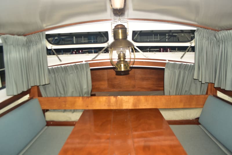 De foto toont het interieur van een boot met een houten tafel, banken met blauwe kussens en een messing lamp. — Doerak 850 AK