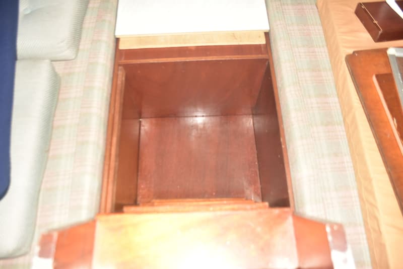 Een open houten opbergvak met een witte plank erboven, omringd door kussens met een geruit patroon.