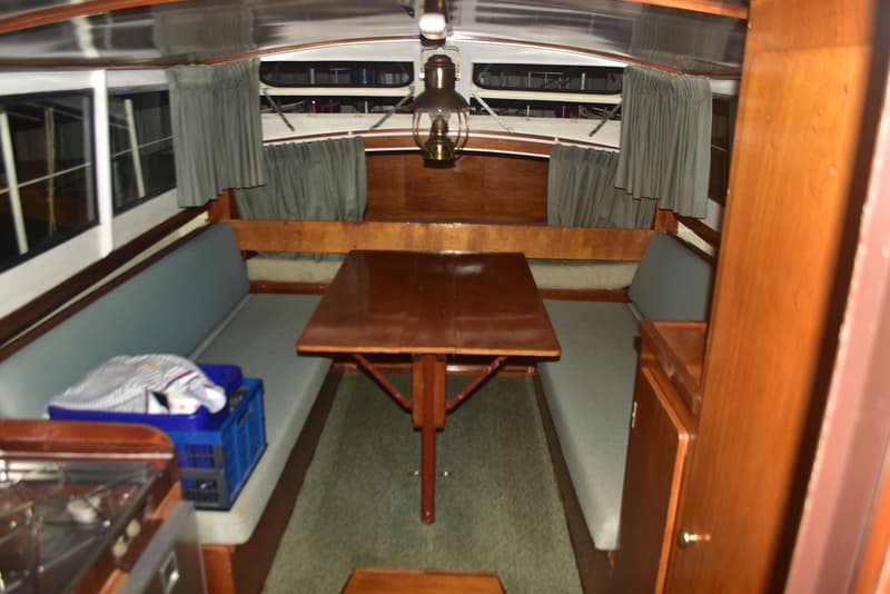 De kajuit van een boot met een houten tafel, banken met lichtblauwe kussens, gordijnen en een kooktoestel. — Doerak 850 AK