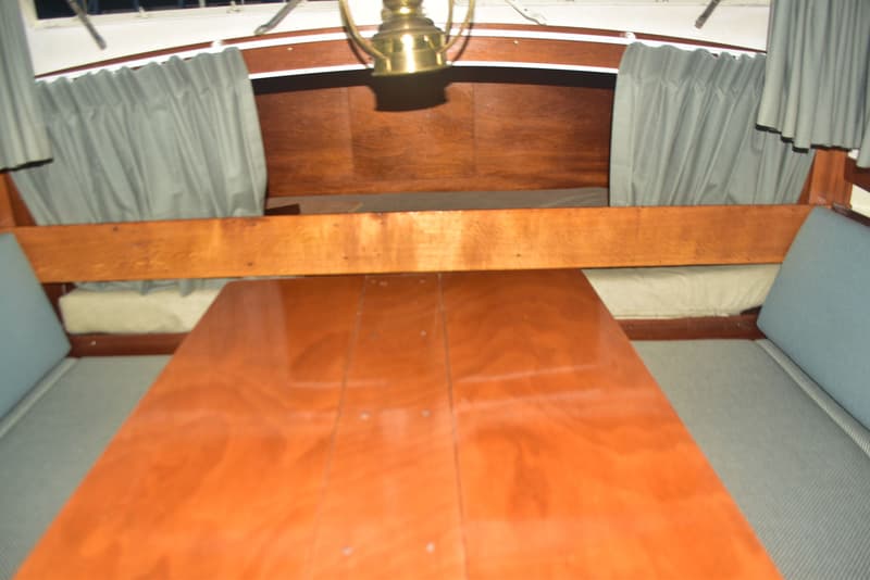 Een houten tafel met twee banken met lichtblauwe kussens en grijze gordijnen in een kajuit. — Doerak 850 AK