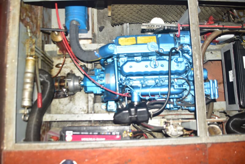 Een blauwe scheepsmotor met diverse slangen en kabels, deels zichtbaar in een motorruimte.