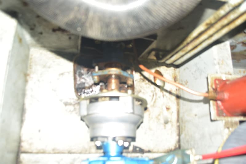 Een close-up van een motorruimte met diverse onderdelen, waaronder een roestige koppeling en bedrading.