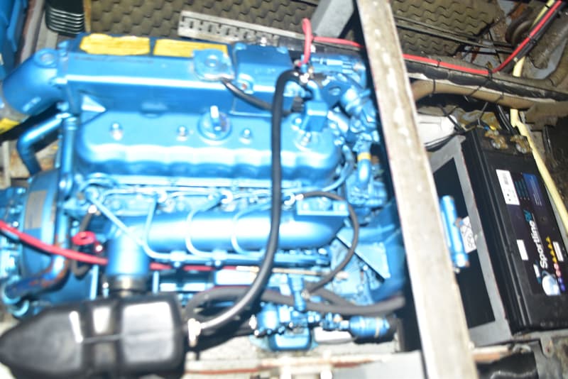 Een blauwe motor met diverse slangen en kabels, en een zwarte accu ernaast.