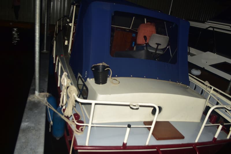 Een boot met een blauw dekzeil en een zwarte emmer op het dek, afgemeerd aan een steiger. — Doerak 850 AK