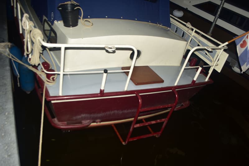 De achterkant van een boot met een donkerrode romp, een wit dek en een blauwe kap, liggend in het water. — Doerak 850 AK
