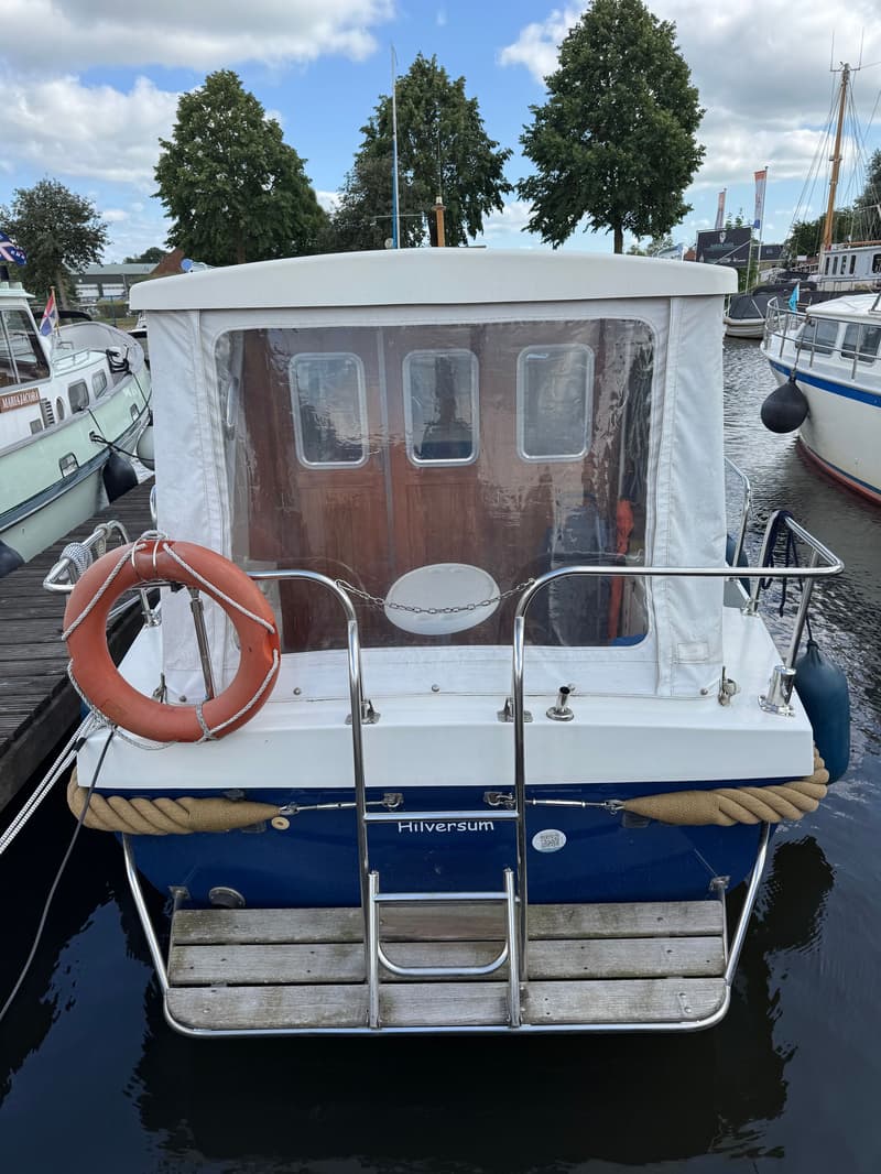 Een blauw-witte boot met de naam "Hilversum" op de spiegel, een zwemplateau en een reddingsboei. — Drammer 8.20 Classic