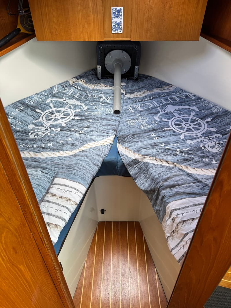 Een kajuit met een V-vormig bed met nautisch beddengoed, een houten vloer en houten kasten. — Drammer 8.20 Classic