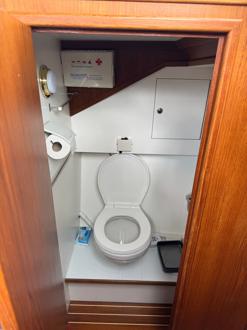 Een toiletruimte met een wit toilet, een verbandtrommel, een toiletrolhouder en houten afwerking.