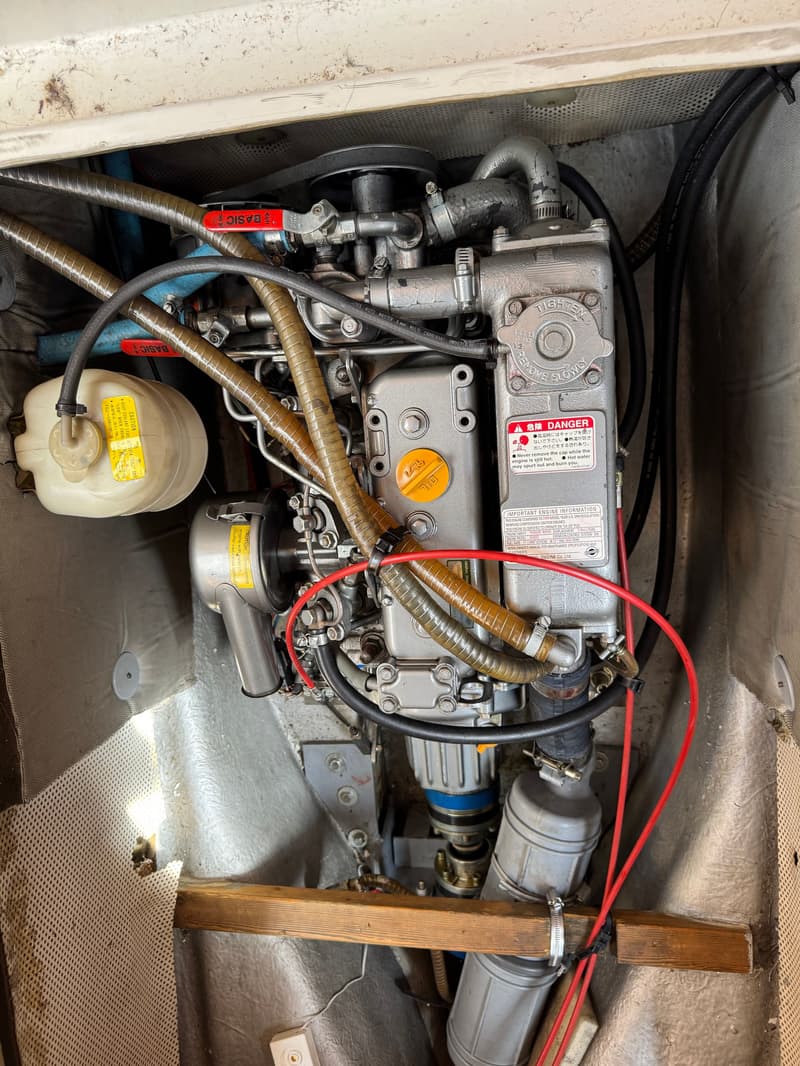 Een close-up van een scheepsmotor met diverse slangen, kabels en een expansievat.