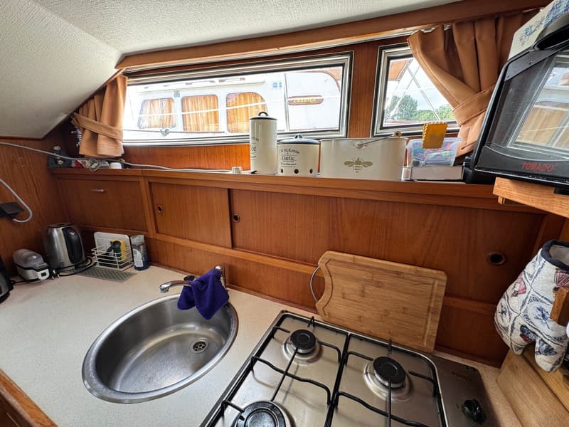 Een bootkeuken met een gootsteen, een tweepits gasfornuis, een waterkoker en een broodrooster.